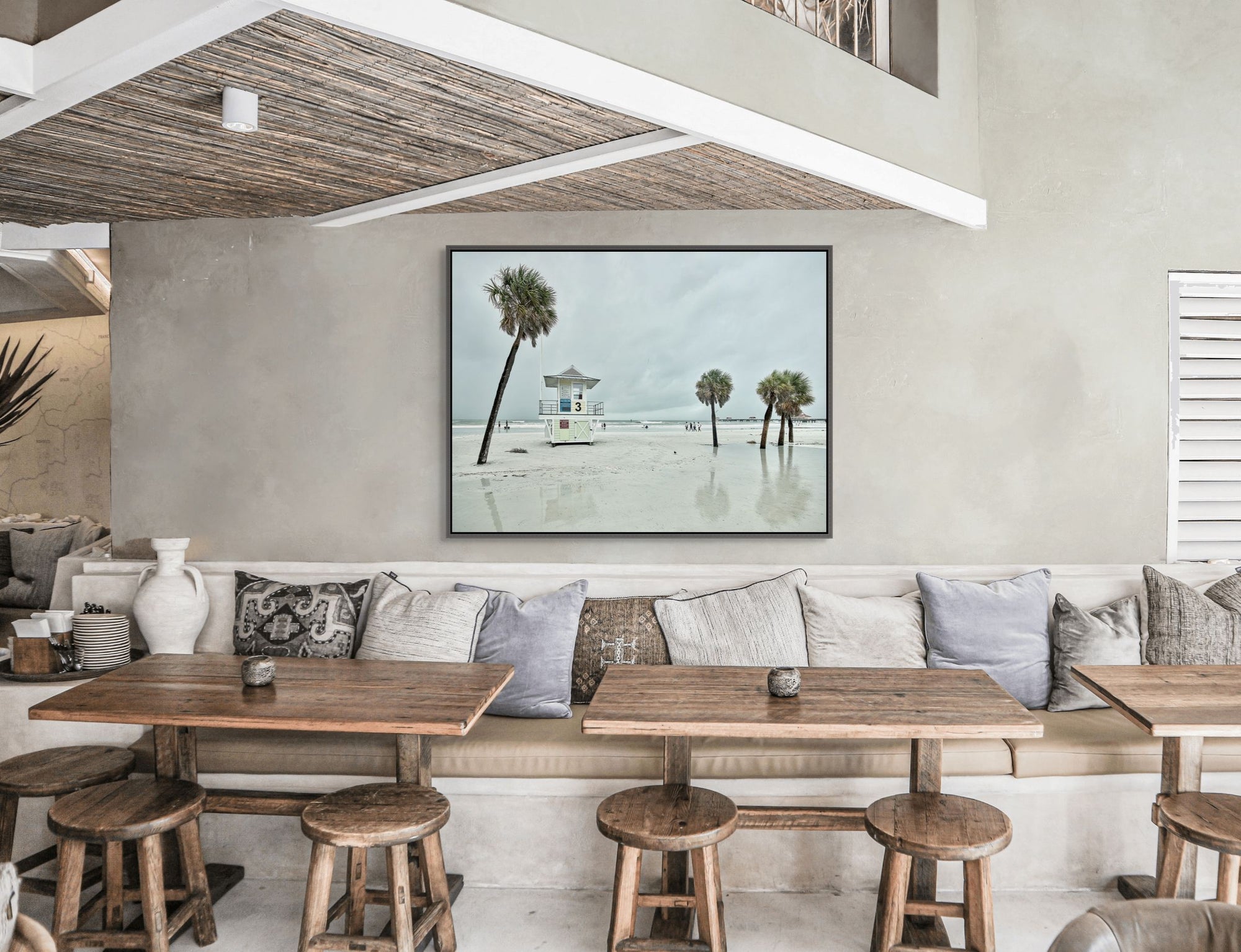 Image of beach with lifeguard stand and palm trees framed over dining tables.