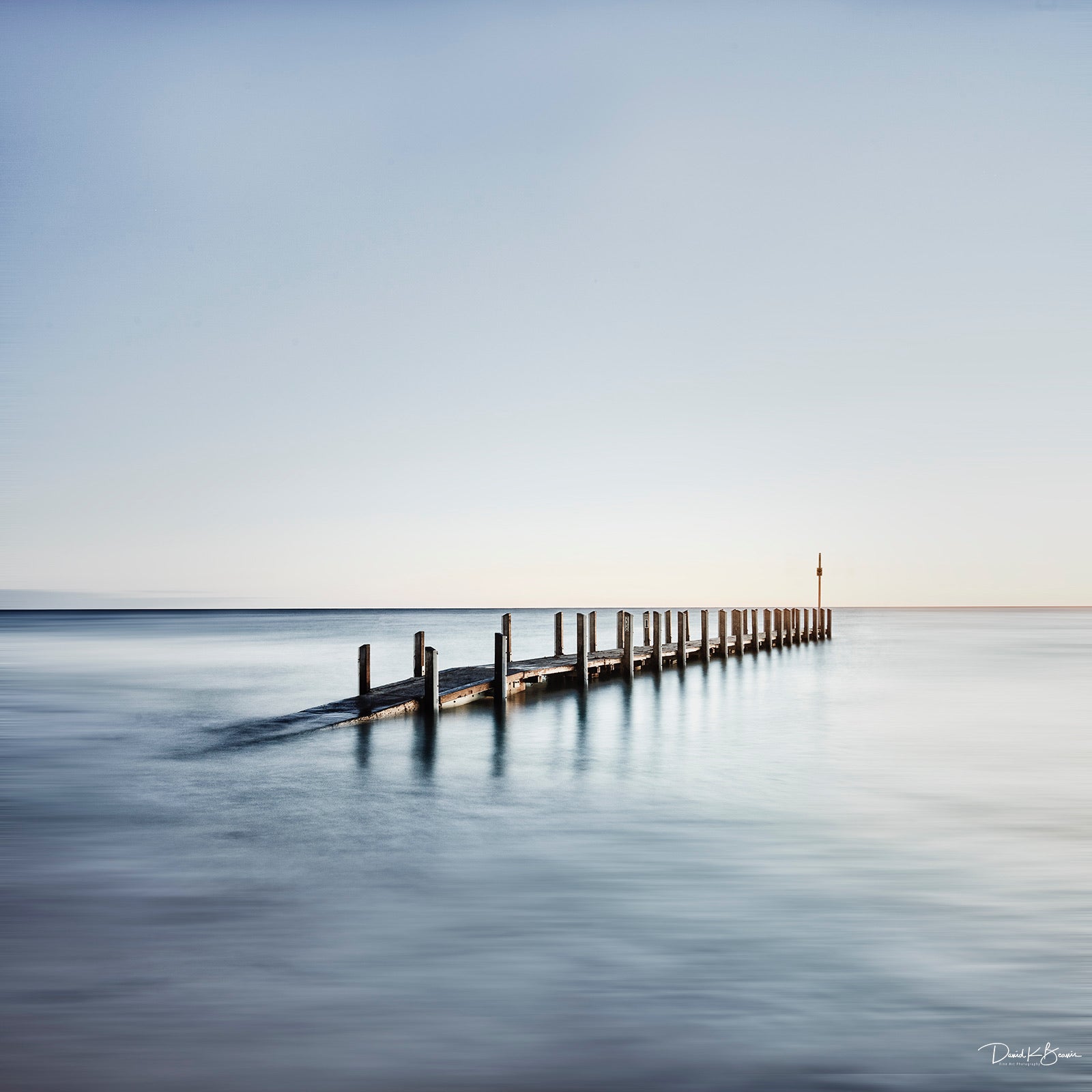 Grey and blue calm waters and wooden dock rising out of the ocean David K Beavis Artist Choice Print High Tide