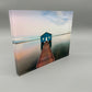 Blue house on a wooden pier over water with a gradient sky.