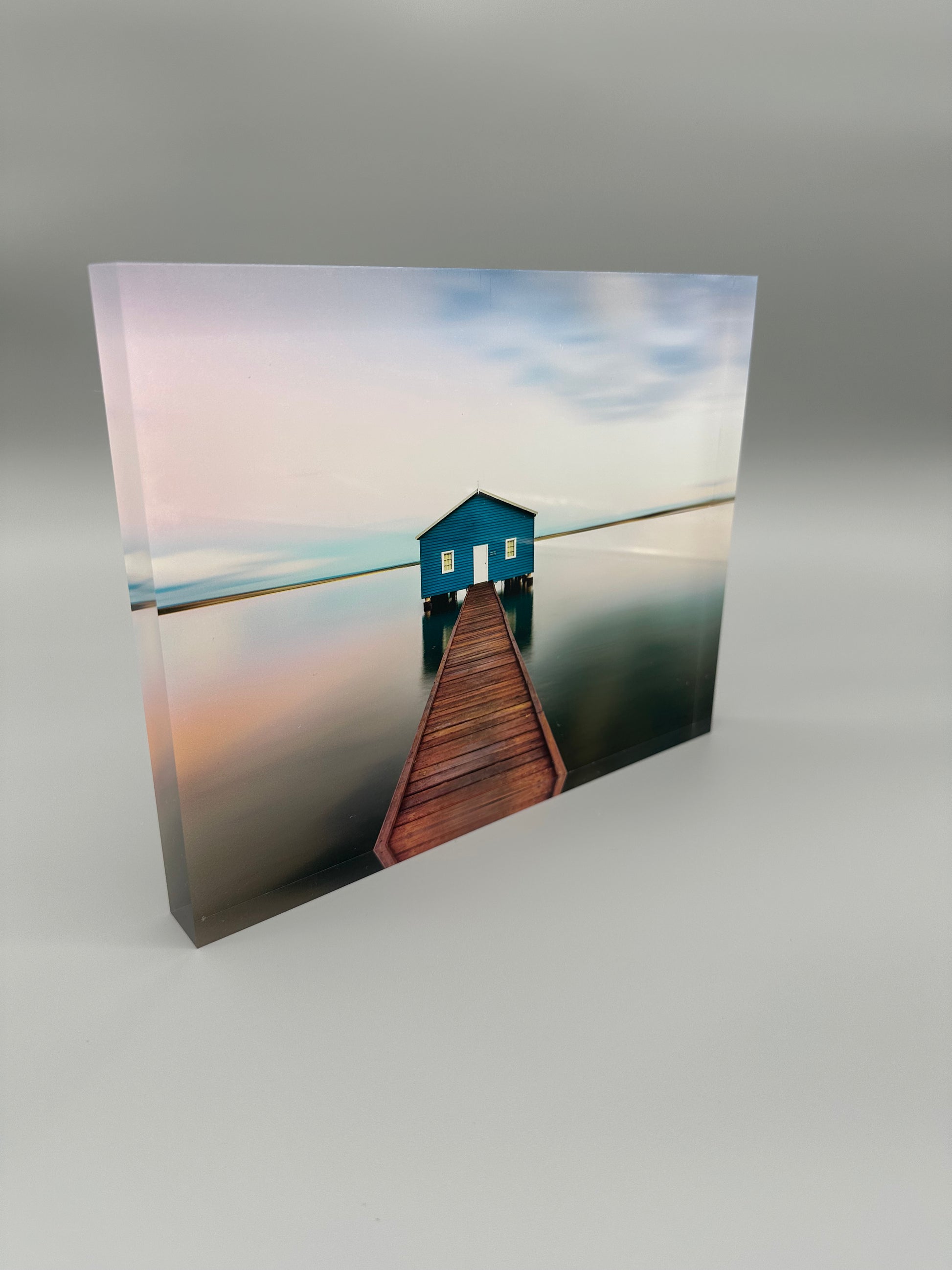 Blue house on a wooden pier over water with a gradient sky.