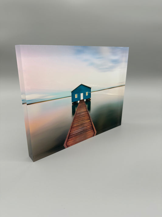Blue house on a wooden pier over water with a gradient sky.