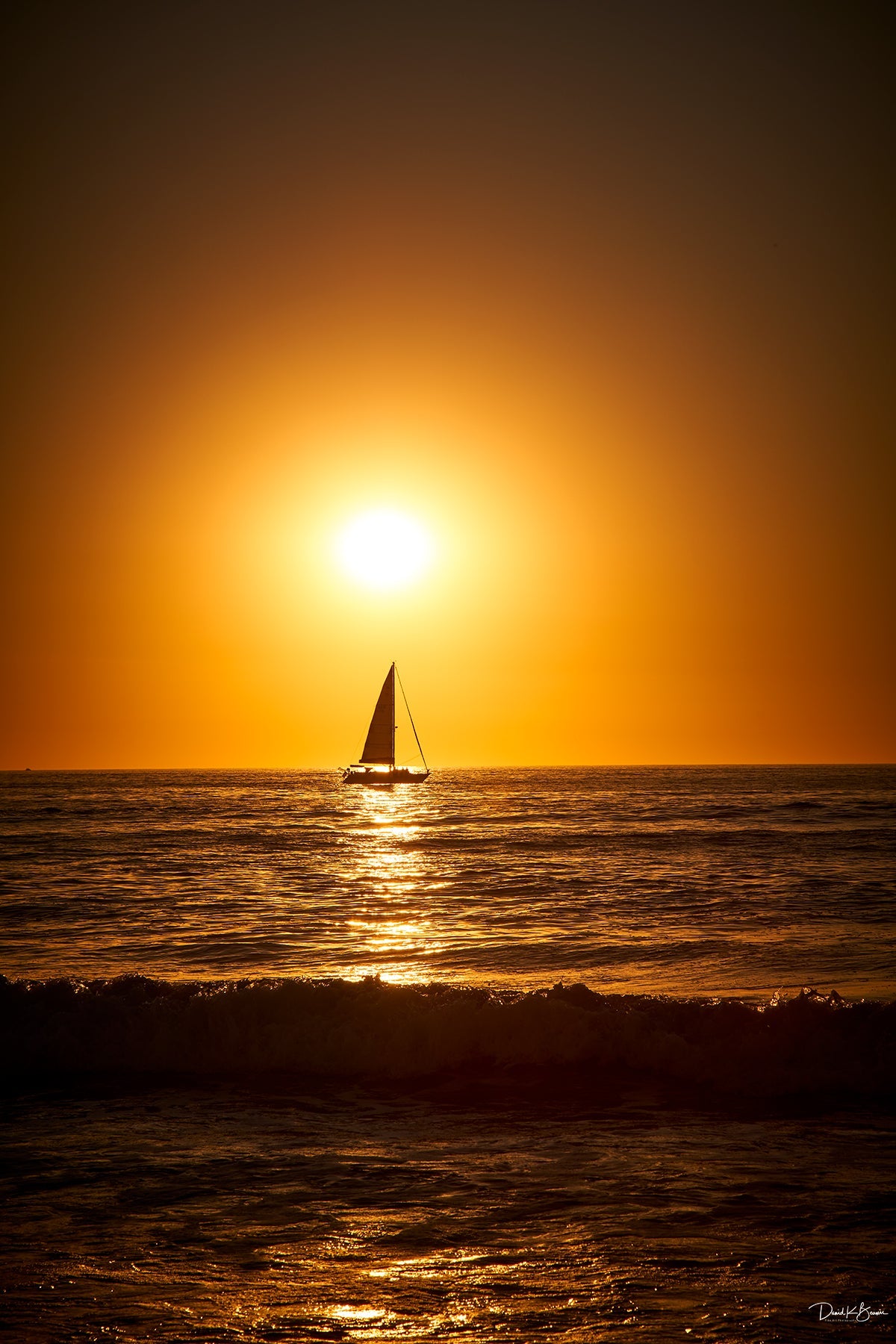 Dark orange sunset over the ocean with the silhouette of a sailboat