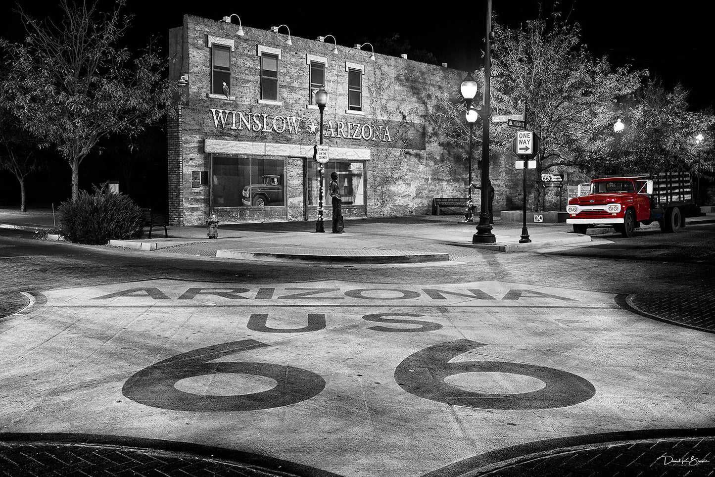 black and white image with building in background,and Arizona US 66 highway sign painted on ground in foreground.
