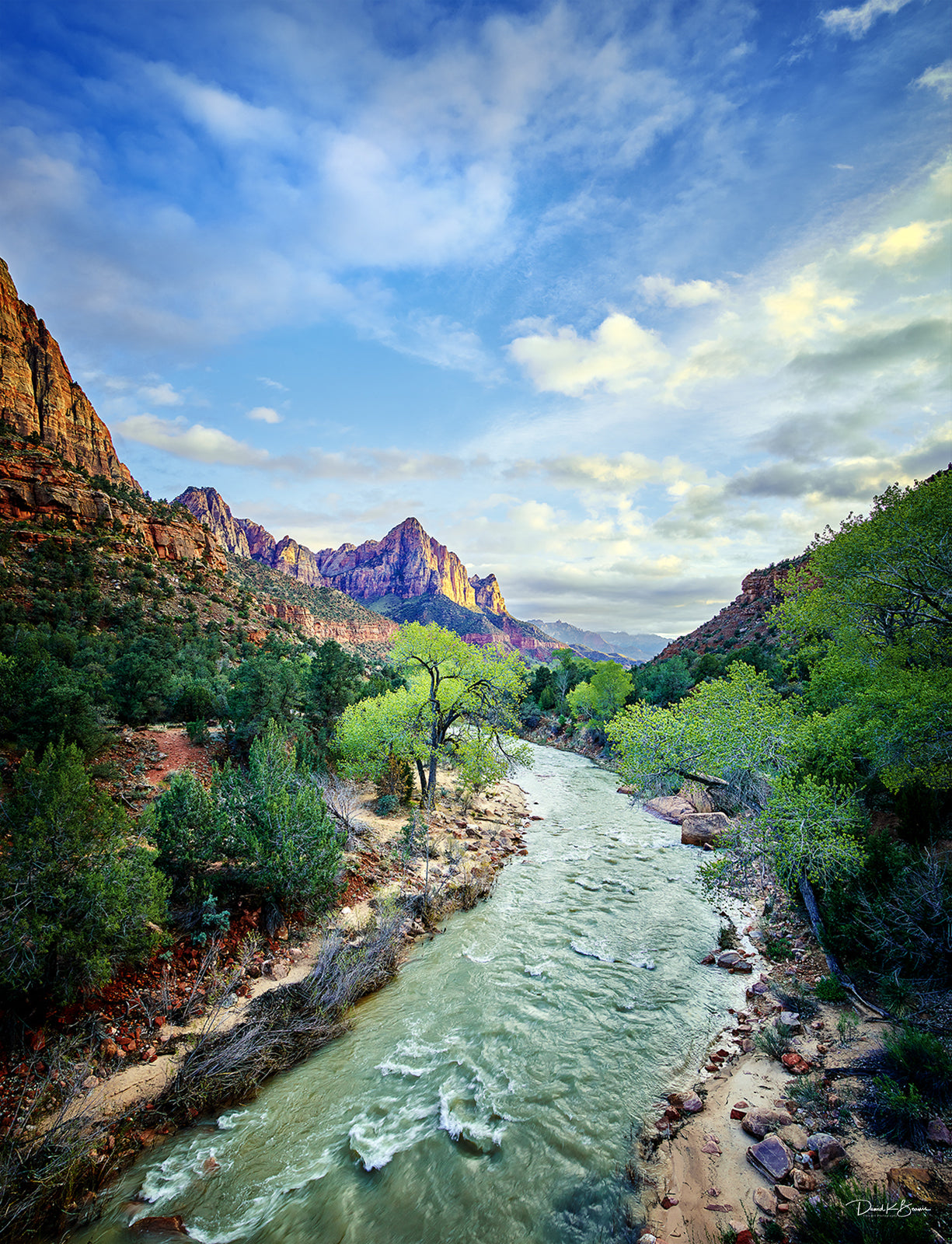 Colorful landscape of mounains with river running through them. Bright green trees follow along the river.